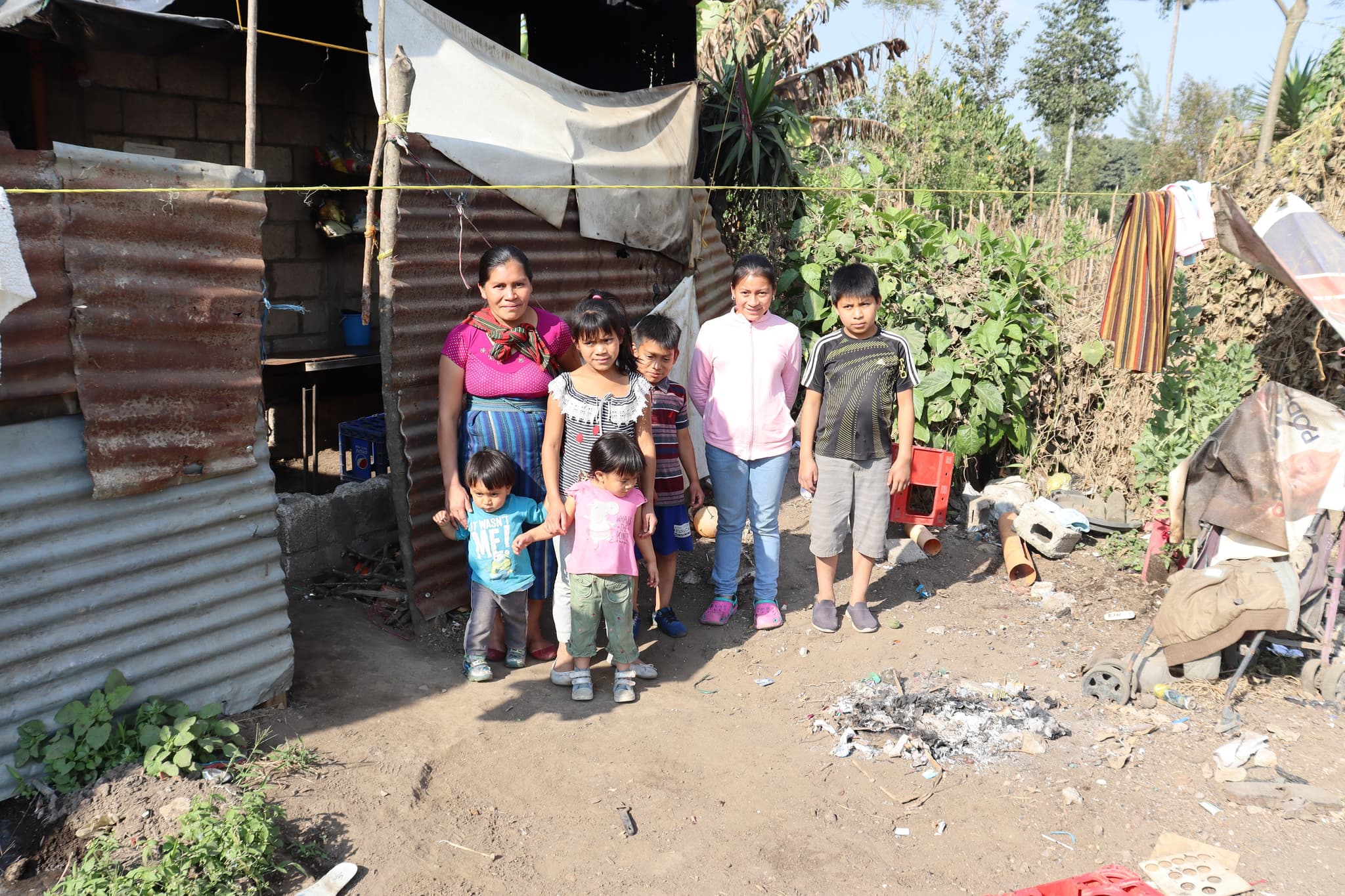 Eine Mutter mit sechs Kindern, die mit ihren Kindern vor einer Wellblechhütte steht.