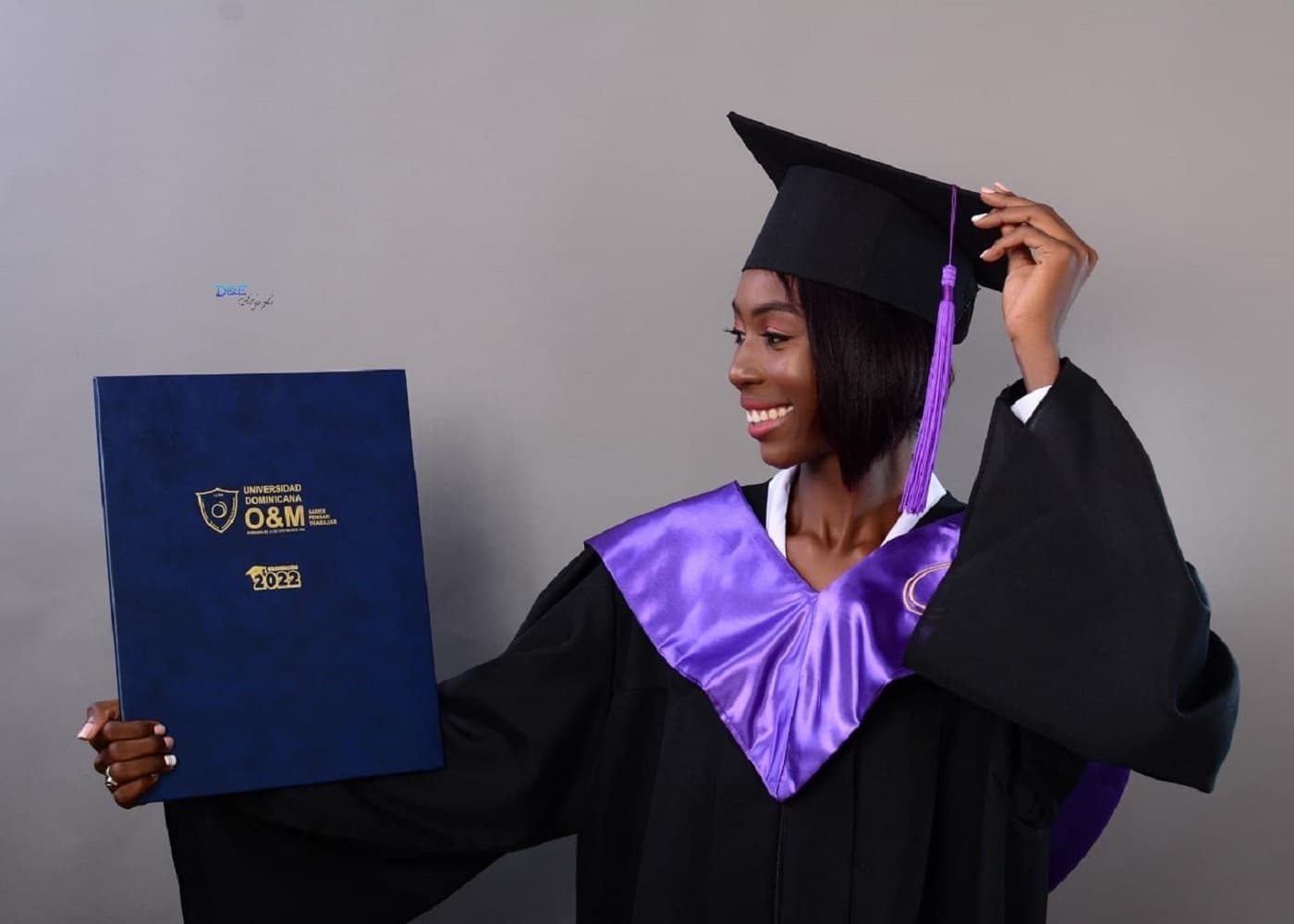 Frau aus Haiti in einer Graduierungs-Garderobe hält ihr Studienzertifikat hoch