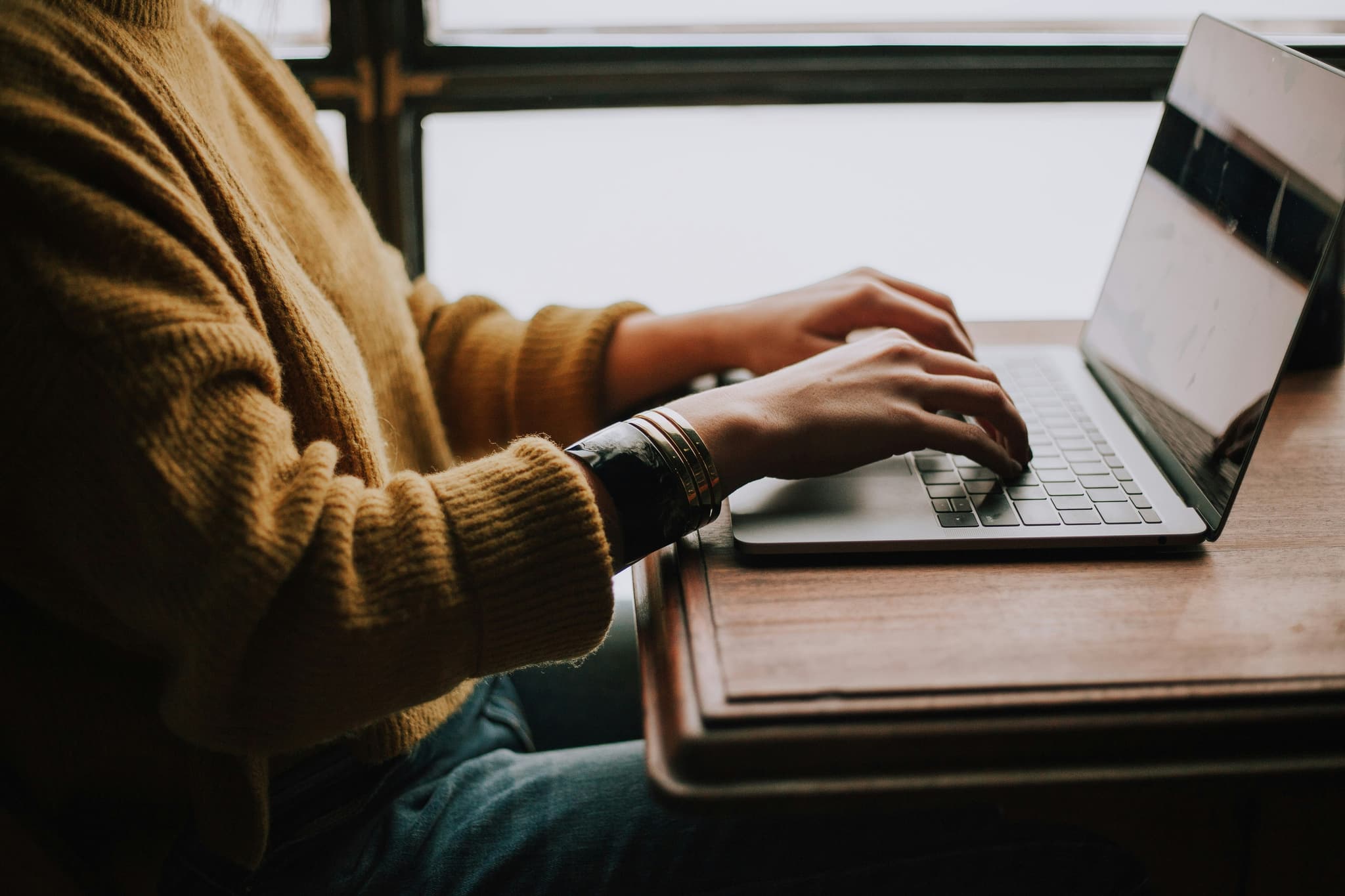 Oberkörper einer am Tisch sitzenden Person, die Hände tippen auf der Laptop-Tastatur