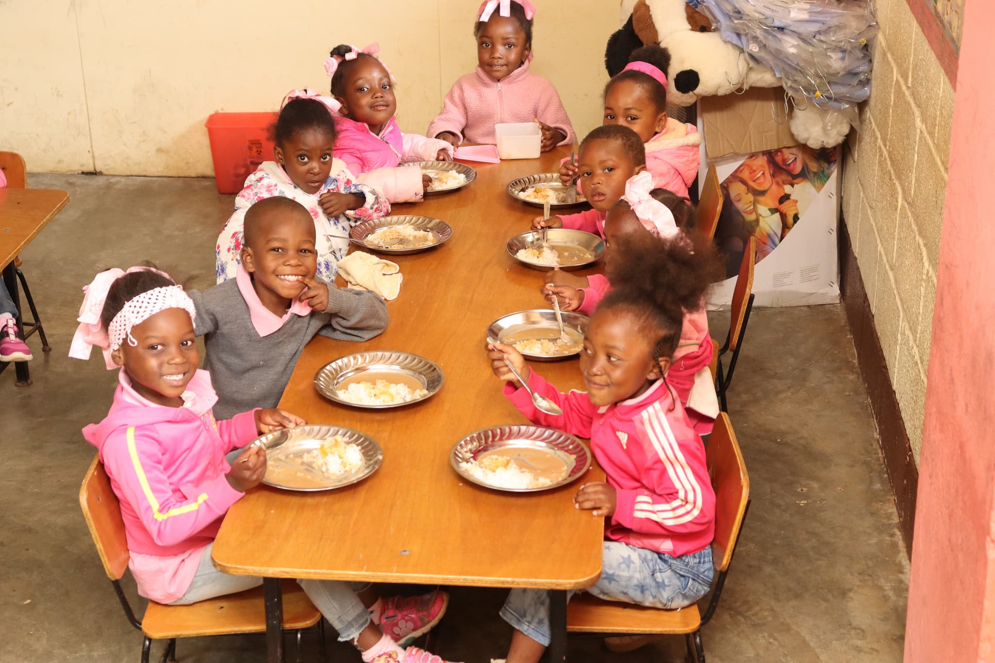 Kinder sitzen um Tisch herum, strahlen und essen