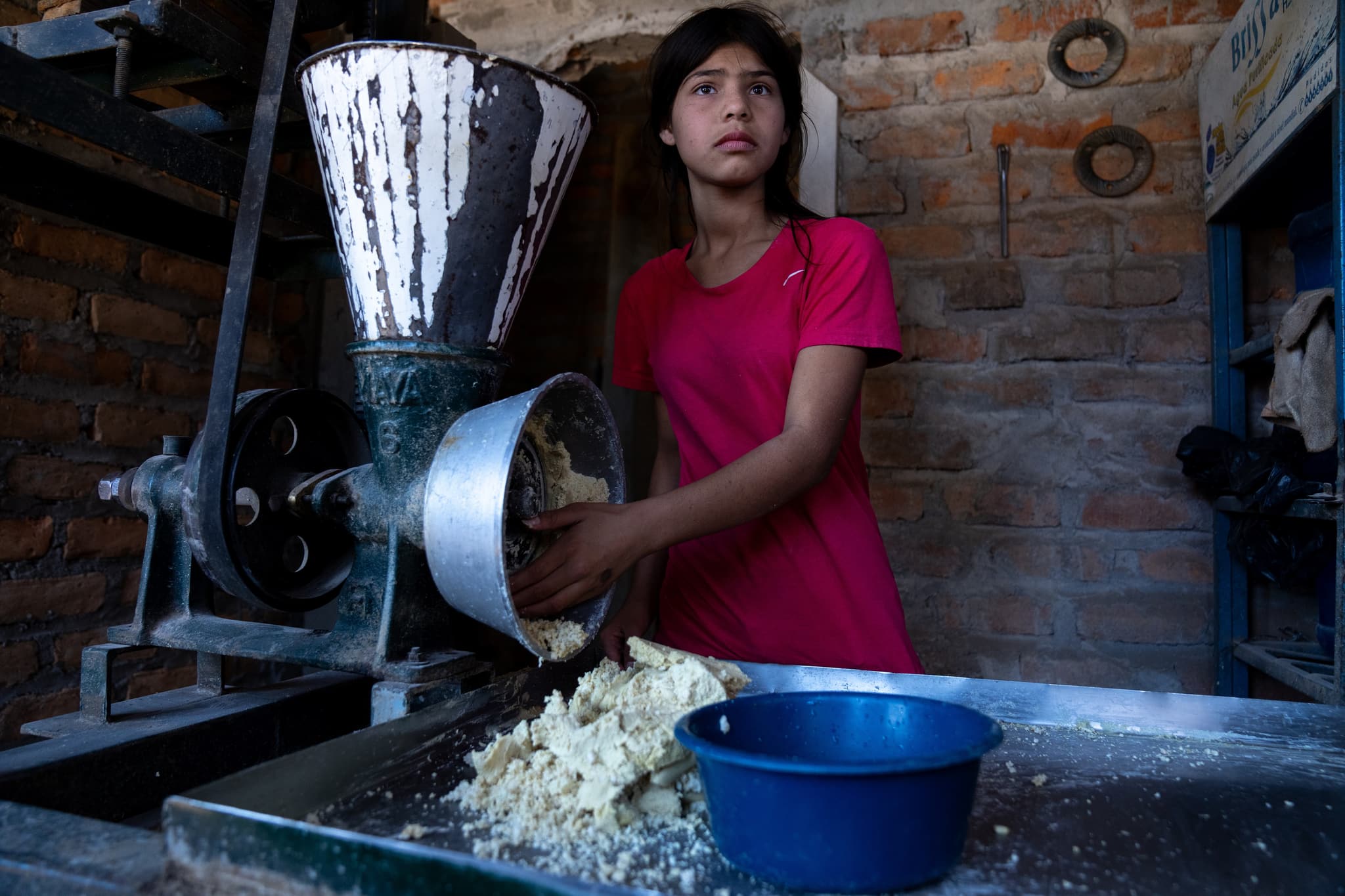 Mädchen aus Honduras, das an einer altmodischen Teigknetmaschine steht und gedankenverloren in die Ferne schaut.