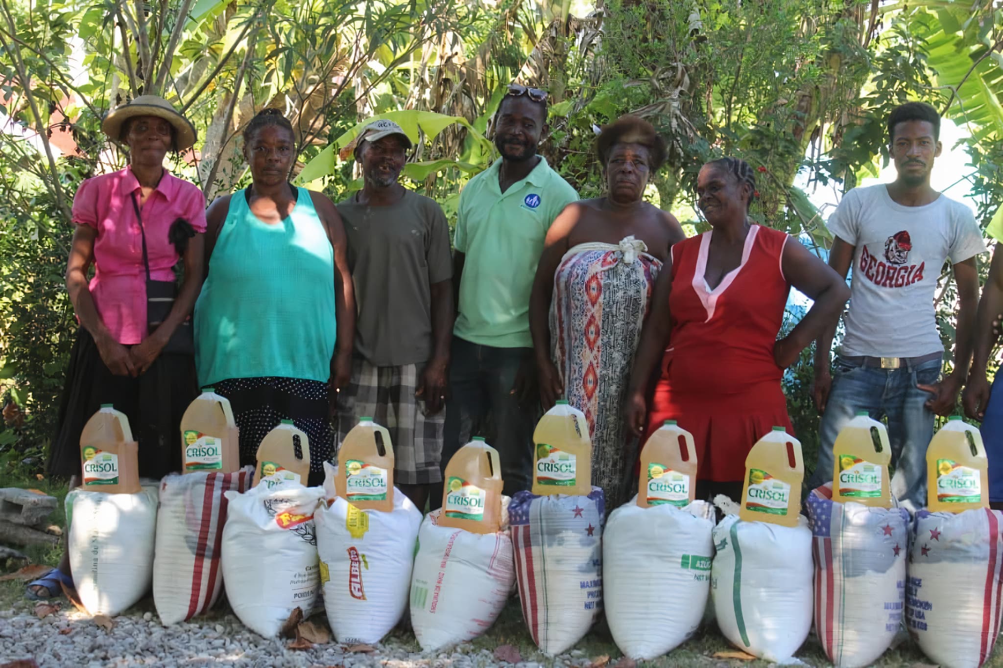 Menschen aus Haiti, die nebeneinander stehen und jeweils einen Reissack und Ölkanister vor sich stehen haben.