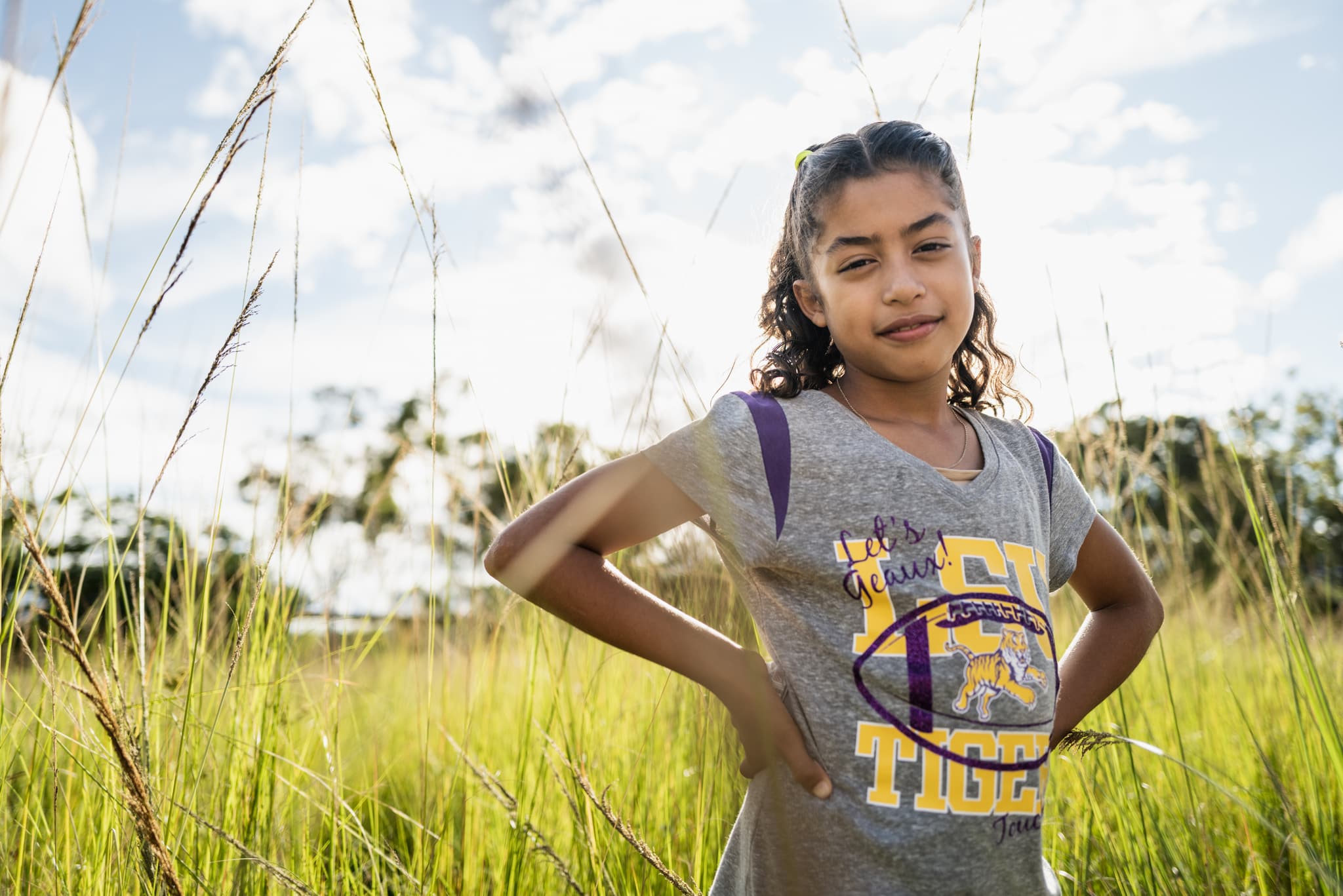 Mädchen mit einem grauen Tshirt, das auf einem Feld steht und die Hände in die Hüfte presst