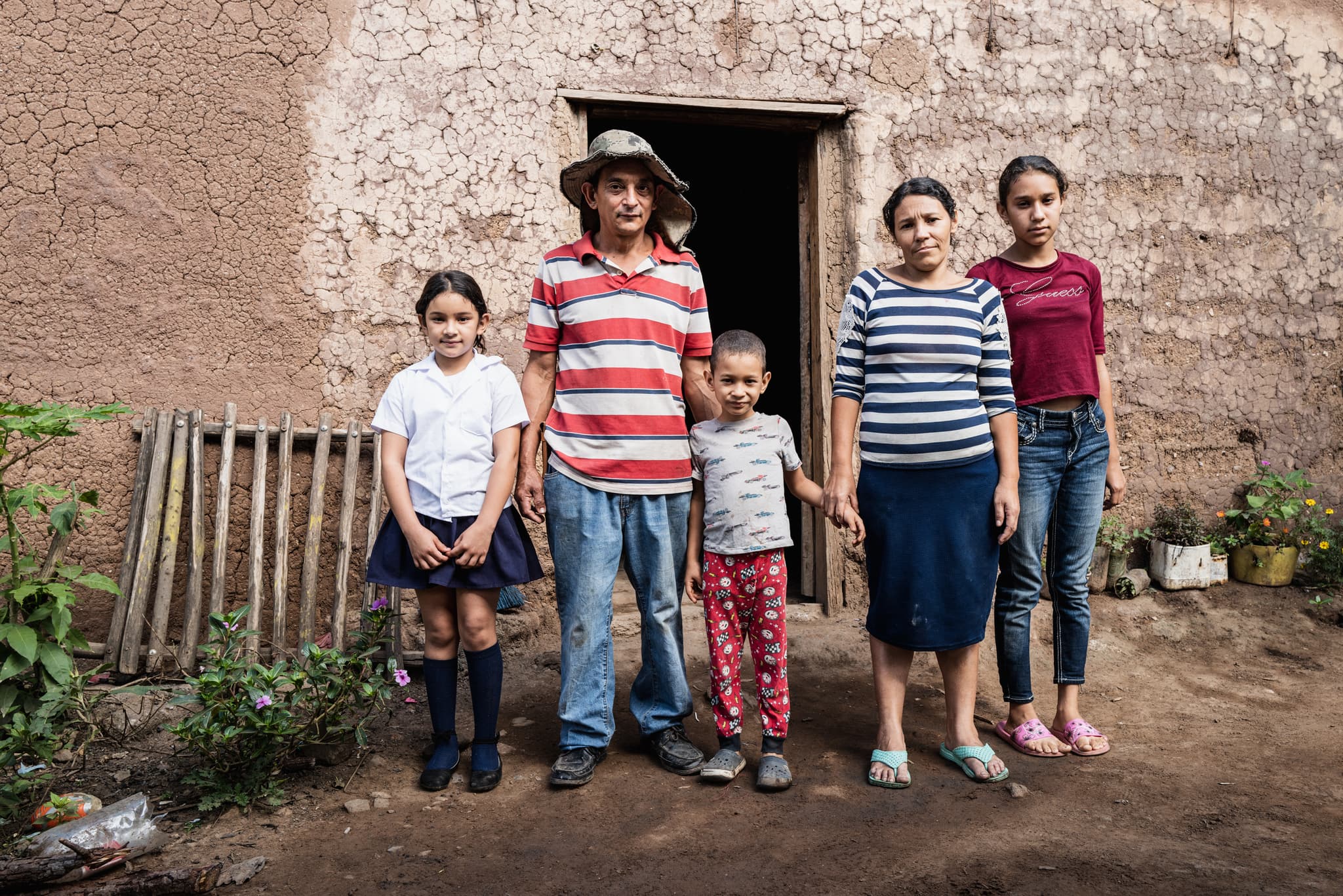 Eine Familie mit Vater, Mutter und drei Kindern, die vor ihrem Zuhause, einer Lehmhütte stehen und traurig aussehen.